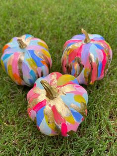 three painted pumpkins sitting in the grass on top of some green grass with gold foil