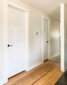 an empty room with white walls and wood flooring is pictured in this image, there are two doors on either side of the hallway