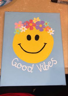 a smiley face painted on a blue canvas with flowers in the middle and words good vibes written below