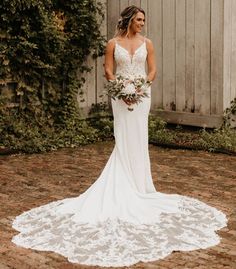 a woman standing in front of a wooden fence wearing a white dress and holding a bouquet