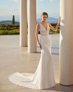 a woman in a white wedding dress standing next to columns and looking at the camera