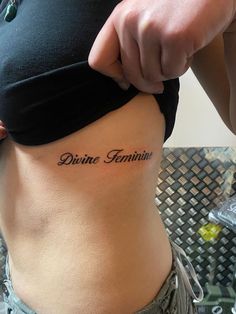 a woman's stomach with the words divine feminine tattooed on her lower side belly