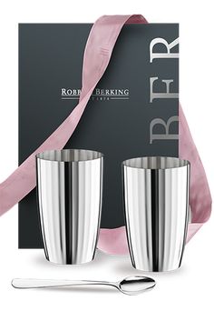 two stainless steel cups with spoons in front of a pink ribbon and black box