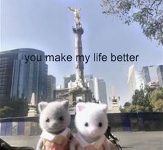 two stuffed animals sitting next to each other in front of a statue with the words you make my life better