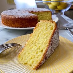 a slice of cake on a plate with a fork next to it and a bowl of lemons in the background