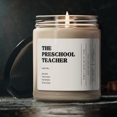 a candle with the words the preschool teacher written on it sitting next to a black mug