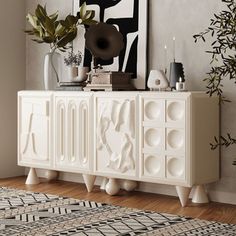 a white cabinet sitting on top of a wooden floor next to a painting and rug