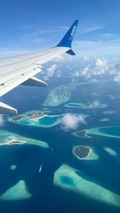 an airplane wing flying over the ocean with many small islands in the water below it