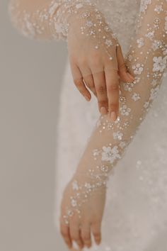 a close up of a person's hand with white flowers on it, wearing a wedding dress