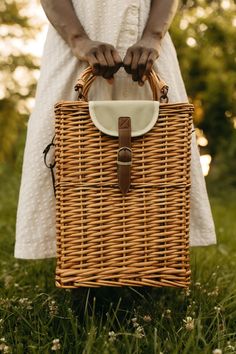 a woman in white dress holding a wicker basket with leather handles and strap around the handle