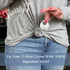 a woman with her hands on her hip wearing a gray shirt and jeans, holding a pair of scissors