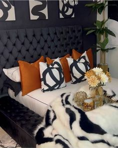 a black and white bed with orange pillows, flowers and vases on the headboard