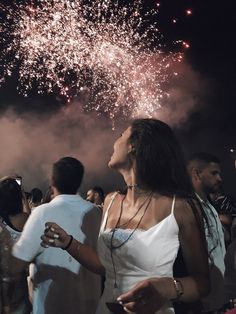 a group of people standing around each other with fireworks in the sky behind them and onlookers watching