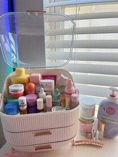 a white container filled with lots of different types of beauty products next to a window