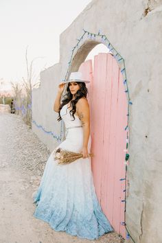 a woman in a white dress and hat leaning against a pink door with lights on it