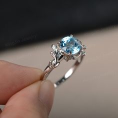 a close up of a person's hand holding a ring with a blue stone