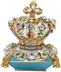 a blue and gold vase with flowers on it's sides, in the shape of a crown