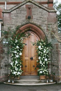 a wooden door surrounded by greenery and candles in front of an old stone building