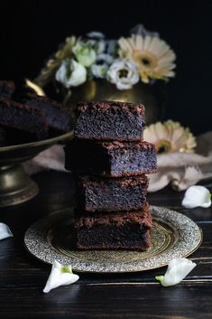 a stack of brownies sitting on top of a plate next to a vase with flowers