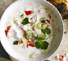 a white bowl filled with cucumber and sauce next to some grilled bread