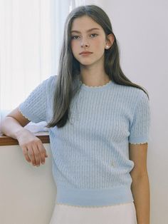 This product is a finely knit, cable-stitched top that combines the classic charm of a sweater with the ease of a t-shirt. It features a delicate contrast trim along the edges, adding a subtle pop of color to the otherwise understated design. The piece is finished with a ribbed hem and cuffs, which contribute to a snug and comfortable fit. - This top's crew neck design offers a timeless look that pairs well with various jewelry and necklines.- The cable knit pattern is meticulously crafted, adding texture and visual interest to the garment.- Its short sleeves make it suitable for warmer days or can be layered during cooler seasons.- A pair of small, decorative buttons at the hem introduces an element of sophistication to the overall design. Elegant Cable Knit Crew Neck Top, Light Blue Fine Knit Top For Spring, Elegant Crew Neck Cable Knit Top, Light Blue Knitted Crew Neck Top, Light Blue Cable Knit Tops, Light Blue Crew Neck Knitted Top, Spring Cable Knit Short Sleeve Tops, Feminine Pointelle Knit Sweater With Crew Neck, Spring Short Sleeve Cable Knit Tops