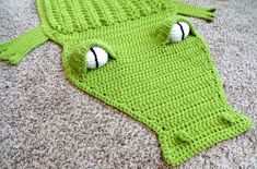 a crocheted green alligator costume laying on the floor with eyes and noseballs