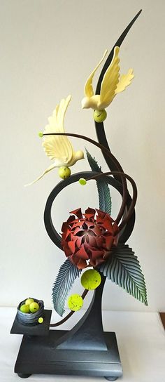 a metal sculpture with flowers and leaves on it's base, sitting on a table