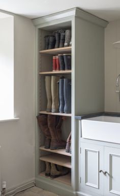 a white sink sitting under a window next to a tall shelf filled with rain boots