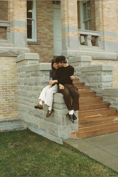 two people sitting on the steps of a brick building with their arms around each other