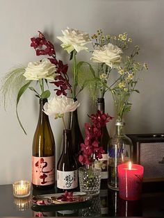 three wine bottles with flowers in them on a table next to a candle and some candles