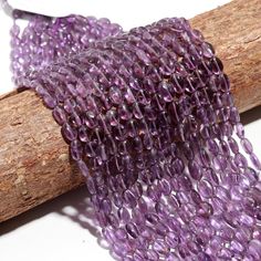 purple glass beads are hanging from a wooden spool on a branch with a white background