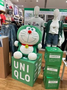 a green and white cat sitting on top of a box in front of clothing mannequins