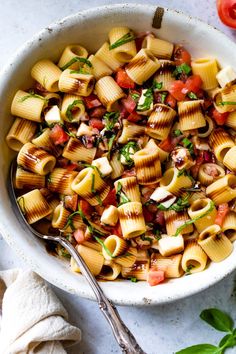 a white bowl filled with pasta salad next to tomatoes and parsley on the side