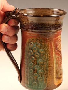 a hand holding a brown and green coffee mug with handles on it's sides