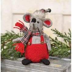 a stuffed mouse in a red dress and scarf on top of a box with pine branches