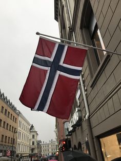 a flag hanging from the side of a building on a street with cars and people