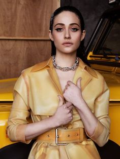 a woman sitting on top of a yellow car with her hands folded in front of her chest