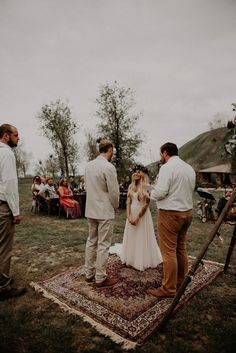 a group of people standing on top of a rug in front of a tree filled field