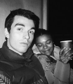 black and white photograph of man and woman holding drinks in their hands while looking at the camera