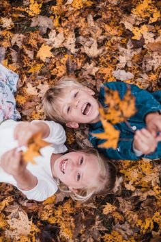 two young children laying on the ground with leaves in their hands and smiling at the camera