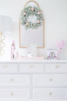 a white dresser with a wreath on top and other items sitting on the drawers in front of it