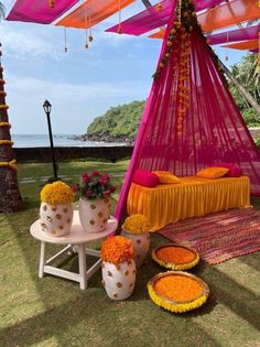 an orange and pink canopy bed sitting on top of a lush green field next to the ocean