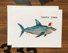 a card with a shark wearing a santa hat on it's head and the words santa jaws written in black ink