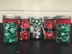 four mason jars filled with candy and christmas decorations, all decorated to look like santa's helpers