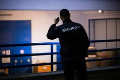 a security man standing in front of a blue door talking on his cell phone at night