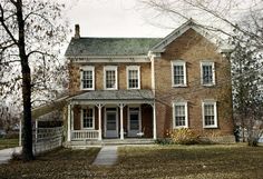 an old brick house with white trim on the front door and porch, surrounded by leafy trees