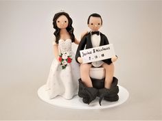 a wedding cake topper with a bride and groom holding a sign