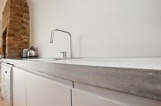 a kitchen with white cabinets and a brick wall behind the sink, in front of a window