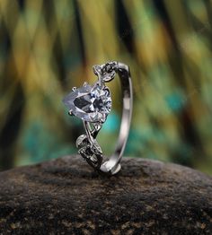 a diamond ring with leaves on it sitting on top of a rock in front of some trees