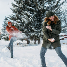 two people playing frisbee in the snow with trees behind them and one person throwing it